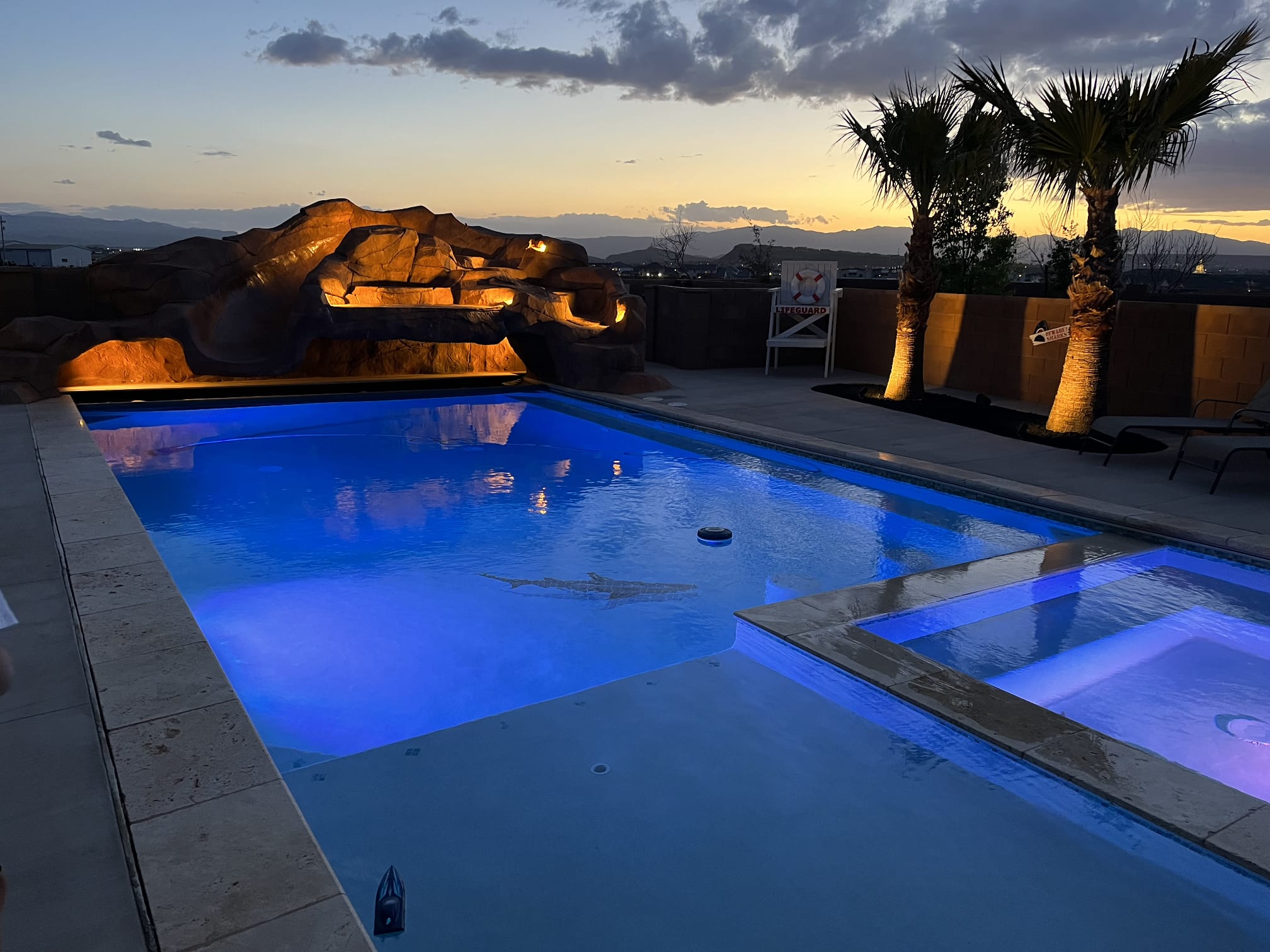 Custom Southern Utah backyard pool with rock waterfall, grotto, slide and spa at sunset — built by Bright Construction Solutions